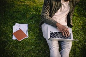 student with laptop and papers on green lawn